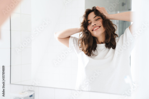 Photo of smiling woman grabbing her head while looking at mirror