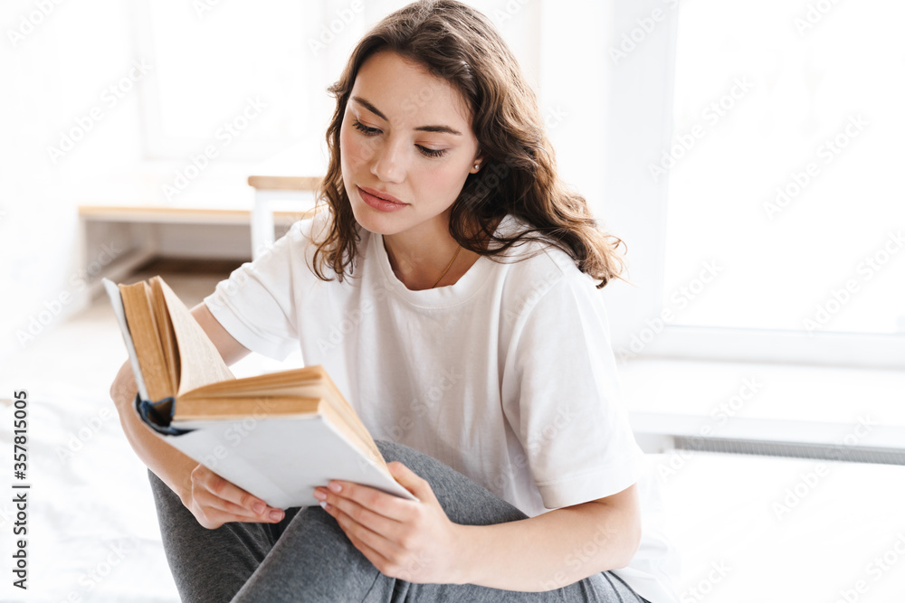 Photo of focused attractive woman reading book while sitting on bed Photo of focused attractive woman reading book while sitting on bed