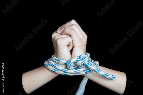 Bound female hands pulling a rope on a black isolated background. Close-up, selective focus, low key, copy space. The concept of kidnapping, hostage-taking, and human trafficking. photo