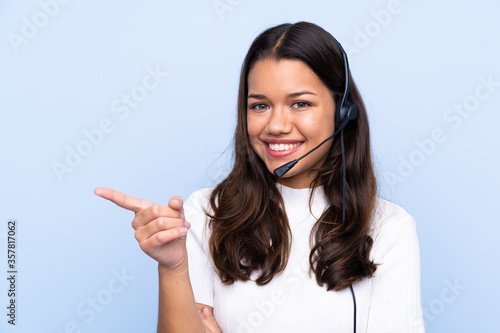 Young telemarketer Colombian woman over isolated blue background pointing finger to the side