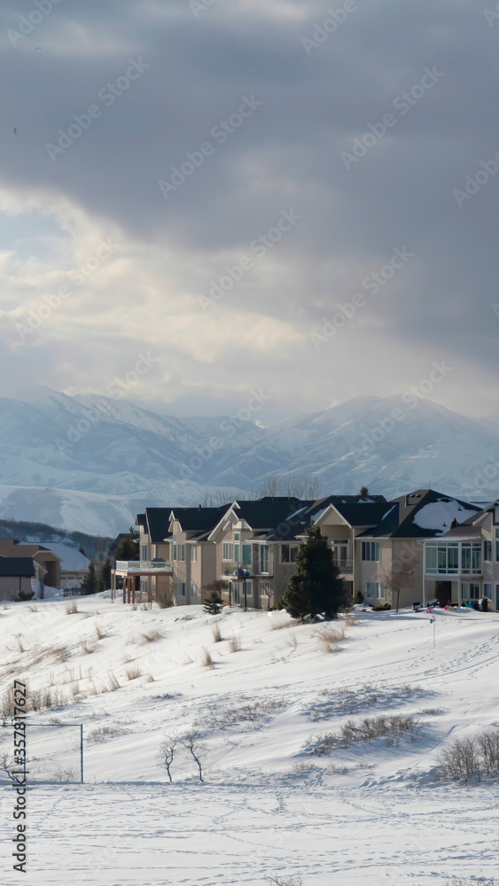 Vertical frame Homes on snowy terrain ovelooking Wasatch Mountain peak and dark overcast sky Vertical frame Homes on snowy terrain ovelooking Wasatch Mountain peak and dark overcast sky