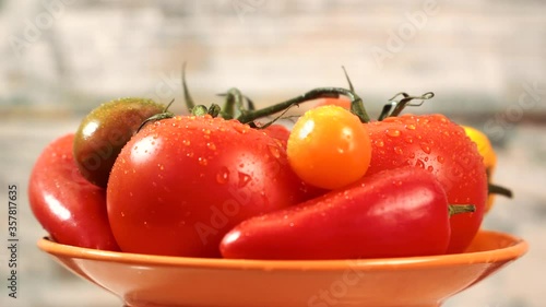 The close-up view of the vegetables, namely the red tomatoes, is yellow, along with the red and yellow peppers, arranged in a saucer. Water drops on vegetables.
