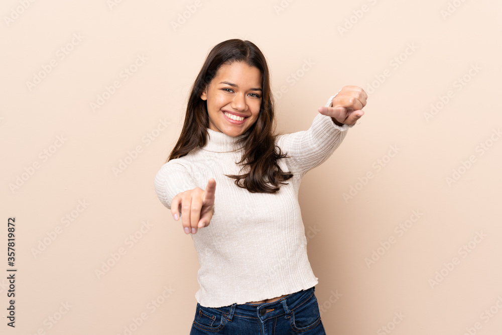 Young Colombian girl over isolated background points finger at you while smiling Young Colombian girl over isolated background points finger at you while smiling