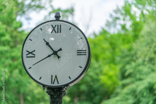 big white street clock on a background of green trees