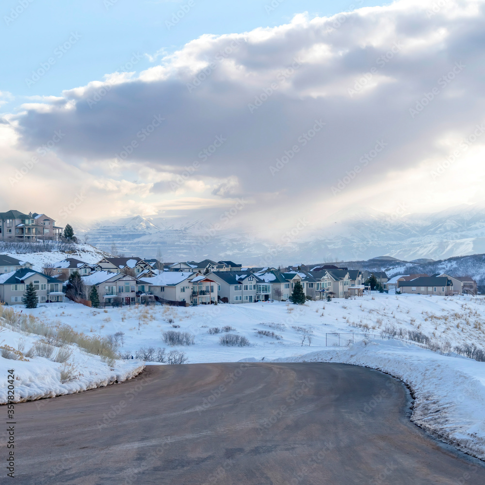 Square Curving road on snowy mountain setting with houses against cloudy blue sky