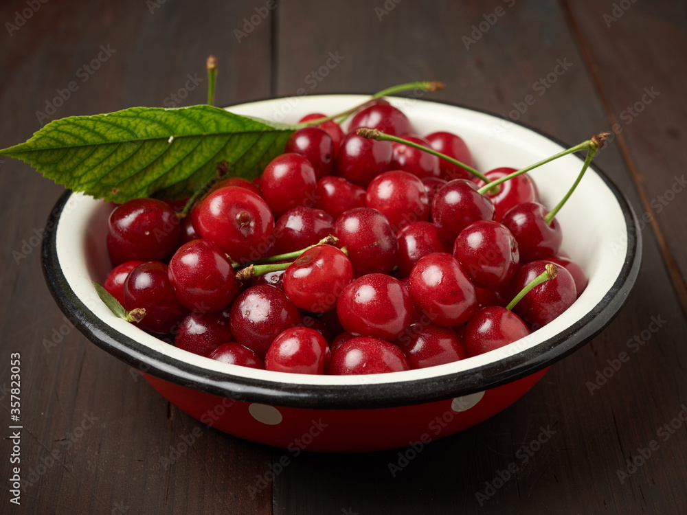 ripe red cherry in a round metal bowl on a brown wooden background ripe red cherry in a round metal bowl on a brown wooden background