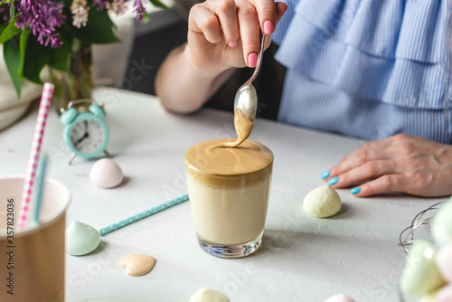 Woman is picking up a spoon and gently stirs the thick whipped mousse in a glass of cold coffee. Gentle atmosphere and sunny beautiful summer morning