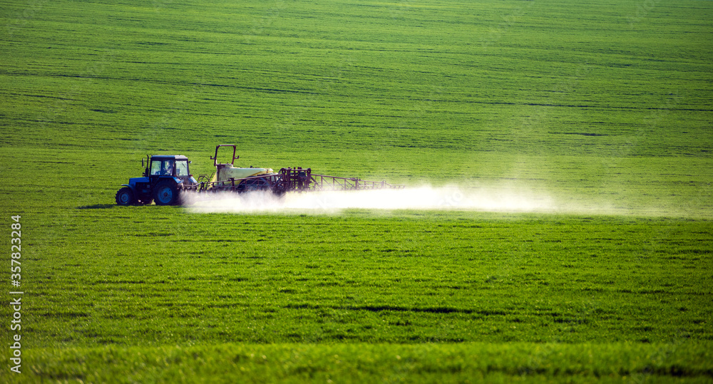 Fototapeta premium Tractor spraying pesticides on field with sprayer at summer