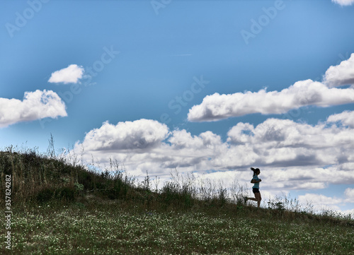Fit athlete woman running down a field hill. Outline of a hill
