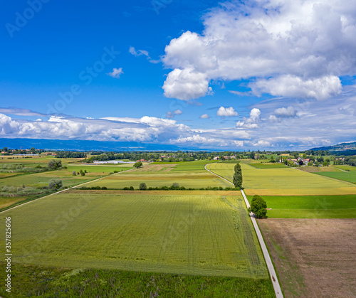 Aerial drone shot of the countryside and farm land around the area of Geneva, Switzerland. The large white clouds and blue sky and green fields of this picturesque landscape.