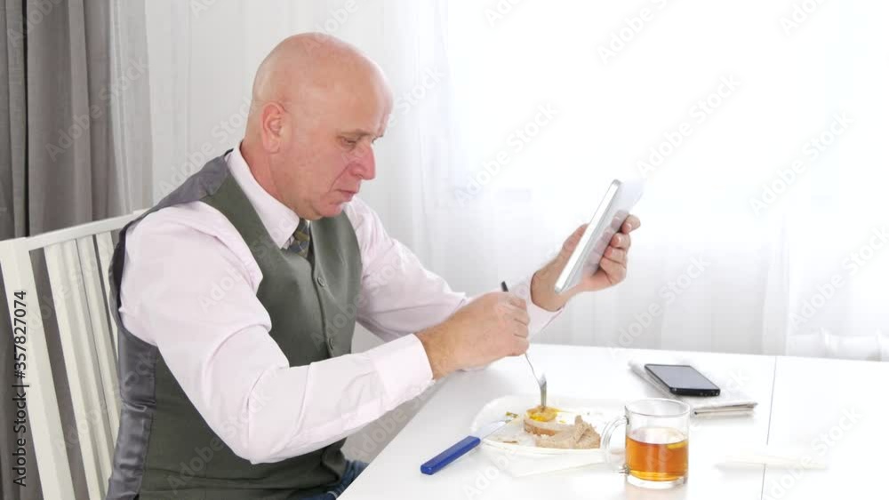 Businessman in a Restaurant Eating and Reading News on Electronic Tablet Businessman in a Restaurant Eating and Reading News on Electronic Tablet