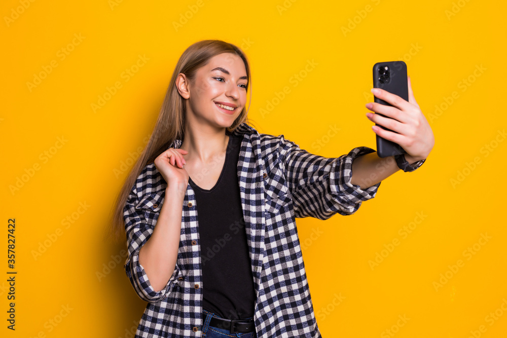 Young pretty woman take selfie on the phone on yellow background Young pretty woman take selfie on the phone on yellow background