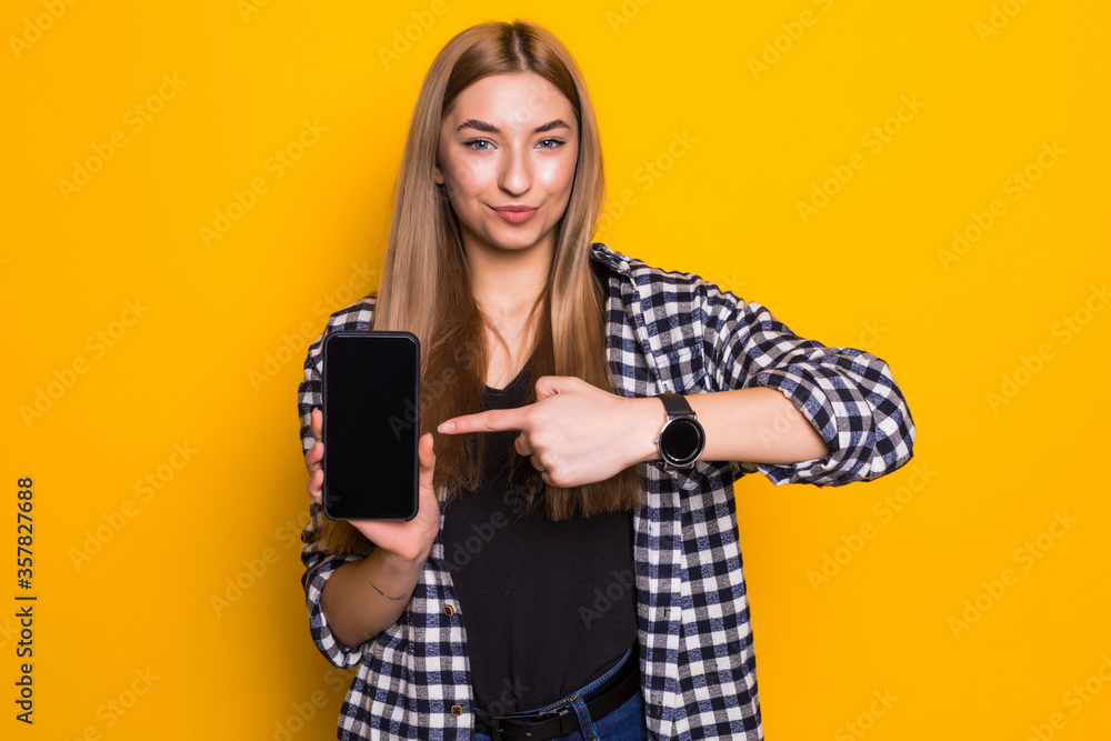 Portrait of a young amazed woman showing blank smartphone screen over yellow background. Portrait of a young amazed woman showing blank smartphone screen over yellow background.