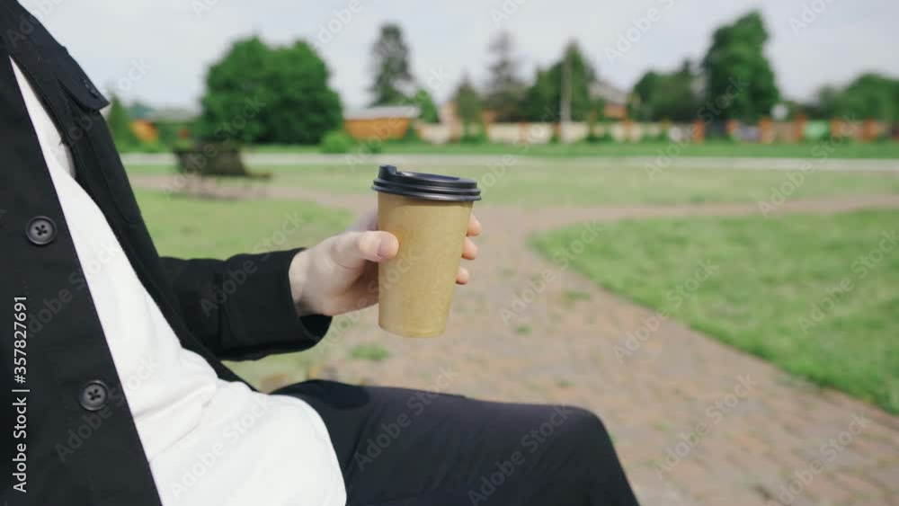 A man sits on a bench holds coffee while walking in the park A man sits on a bench holds coffee while walking in the park