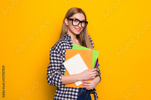 Young woman in glasses holding books in his hands and smiling on a yellow background. concept of study, students