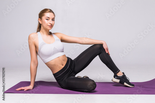 Young fit woman sitting on the matt and relax on white background