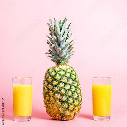  Fresh ripe pineapple and two glasses of pineapple juice on a pink background. hot summer concept. copy space, minimalism. square photo.