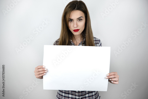 Beautiful young brunette women with banner sign with white blank empty paper billboard with copy space for text over gray background