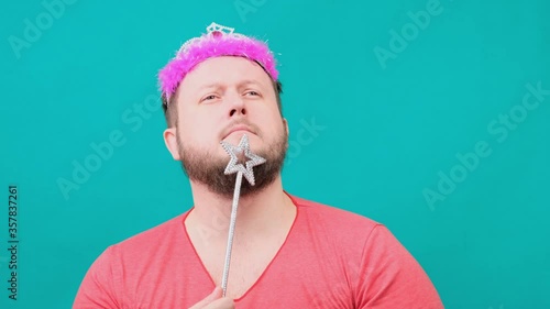 funny bearded freaky man in a pink T-shirt with a deadema on his head is dreaming with a magic wand in his hand. A funny wizard joke to make and fulfill a wish. photo