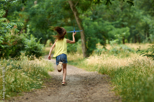 The concept of dreams and travel. Happy girl kid playing with toy airplane in summer on nature.