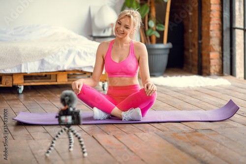 girl seating on yoga mat in sport outfit with camera