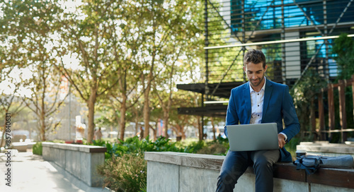 Obraz na plátně Businessman using a laptop while sitting outside his office building