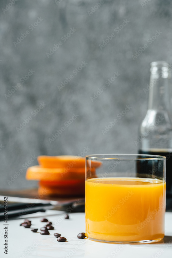 selective focus of orange juice in glass near cold brew coffee and coffee beans on white table selective focus of orange juice in glass near cold brew coffee and coffee beans on white table