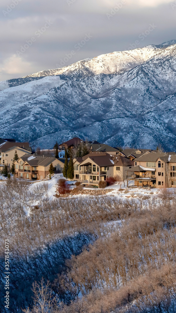 Vertical crop Homes on snowy terrain of Wasatch Mountains with sunlit peak in the background
