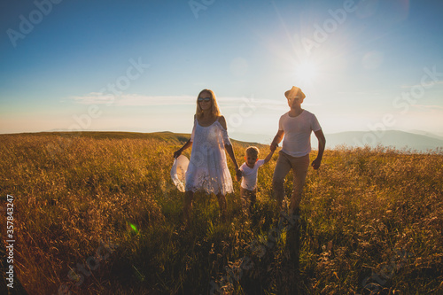 Sunny summer field with cheerful family walking through