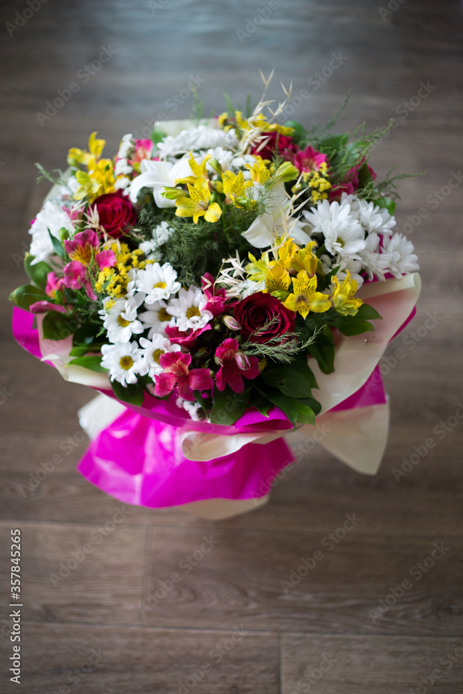 on a dark background, a bouquet of freshly cut flowers in pink wrapping paper. there are many different types of flowers in the bouquet.