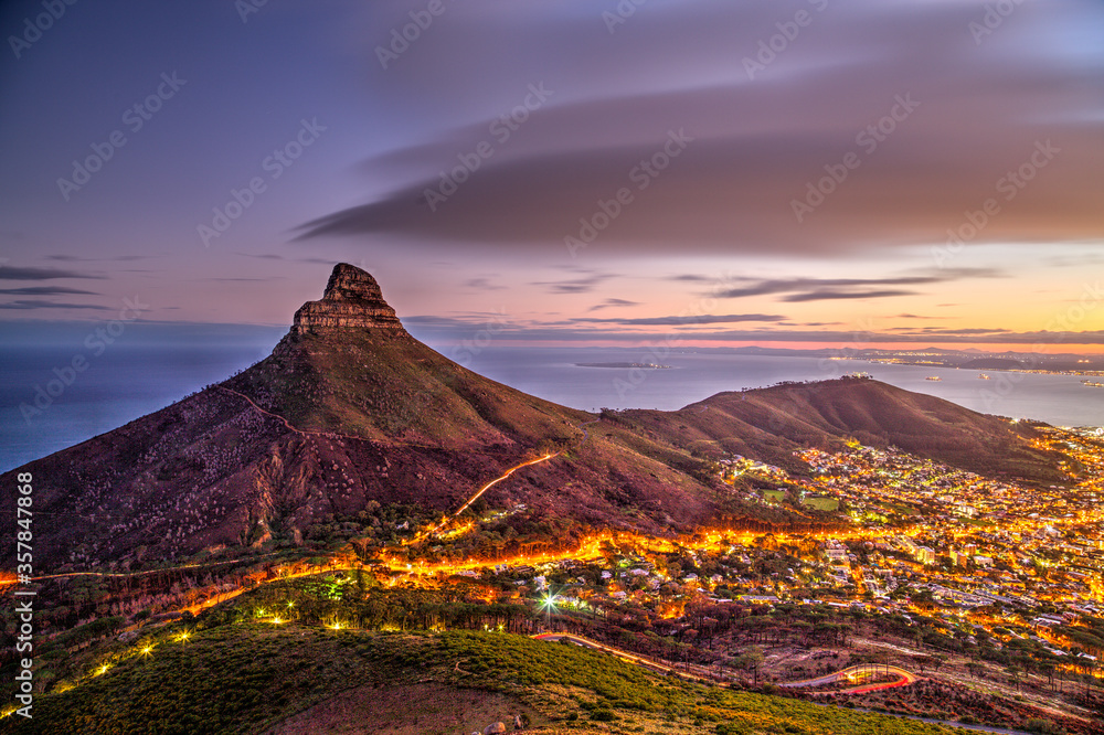 Fototapeta premium Lion's Head A city scape of the landmark Lion's Head in Cape Town, South Africa, just before sunrise. A slightly longer exposure shows some movement in the clouds and car lights.