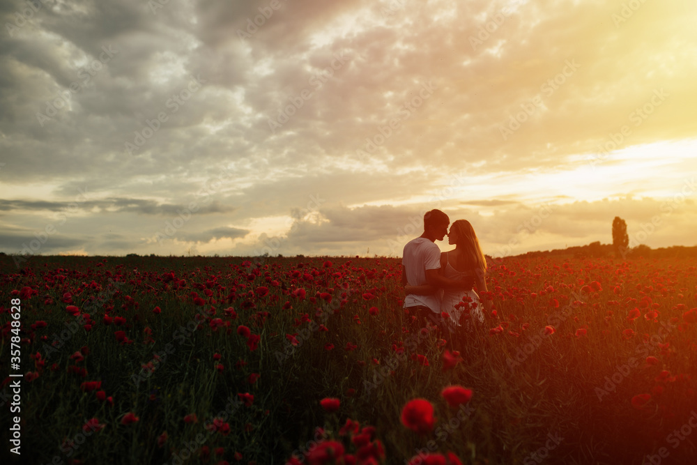 Amazing sunset in the poppy field. Loving couple in the poppy field. The concept of youth, love and lifestyle. Man and woman embracing and kissing in poppy field on the dusk. Copy space.