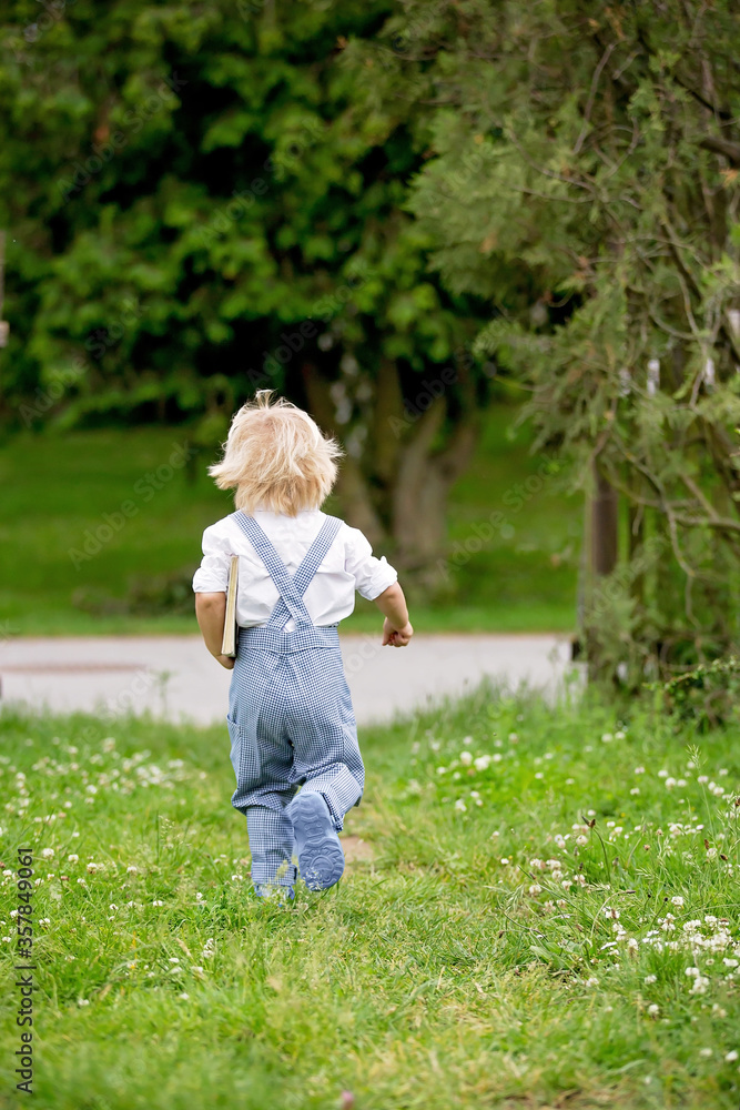 Blond toddler boy in vingate clothes holding book, standing on the street waiting for a bus Blond toddler boy in vingate clothes holding book, standing on the street waiting for a bus