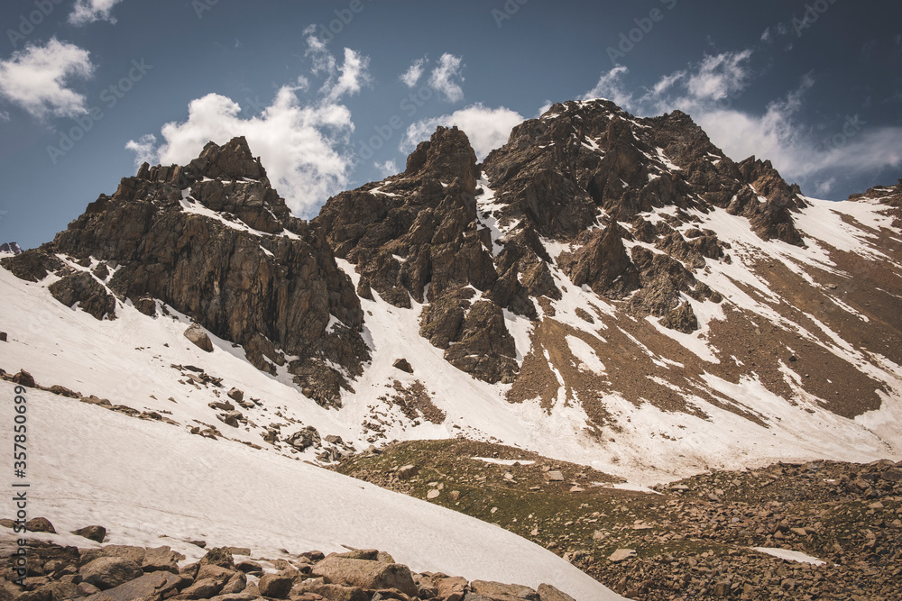 Tien Shan system in Kazakhstan near the city of Almaty. Rocky peaks covered with snow and glaciers in the middle of summer under clouds