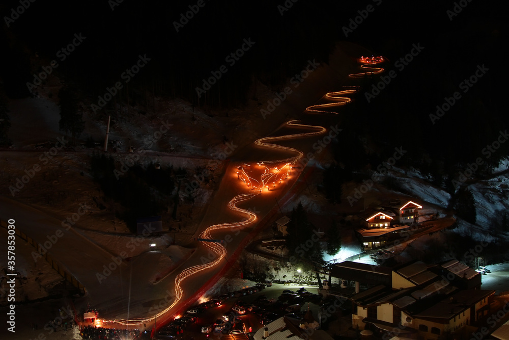 Night long exposure shot of winter ski show. Skiers with torches sliding down and creating a heart in the middle of the slope. Santa Cristina. Val Gardena. Italy.