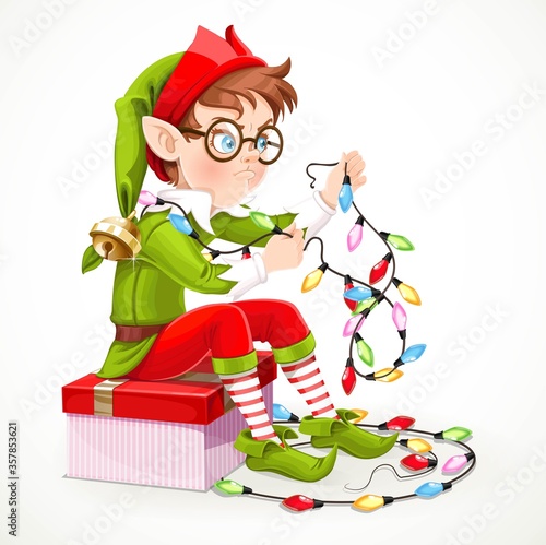 Cute boy elf sitting on a box with a gift and unravels a Christmas garland isolated on white background