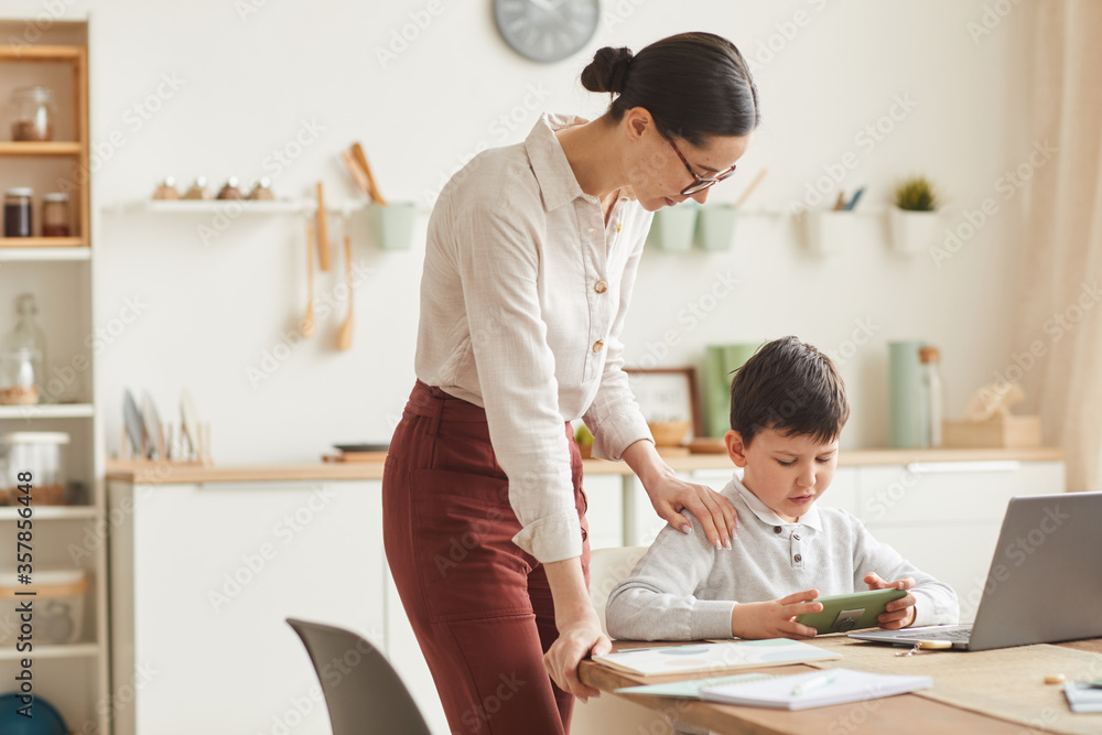 Warm-toned portrait of young mother helping boy trying to study at home in cozy interior, copy space Warm-toned portrait of young mother helping boy trying to study at home in cozy interior, copy space