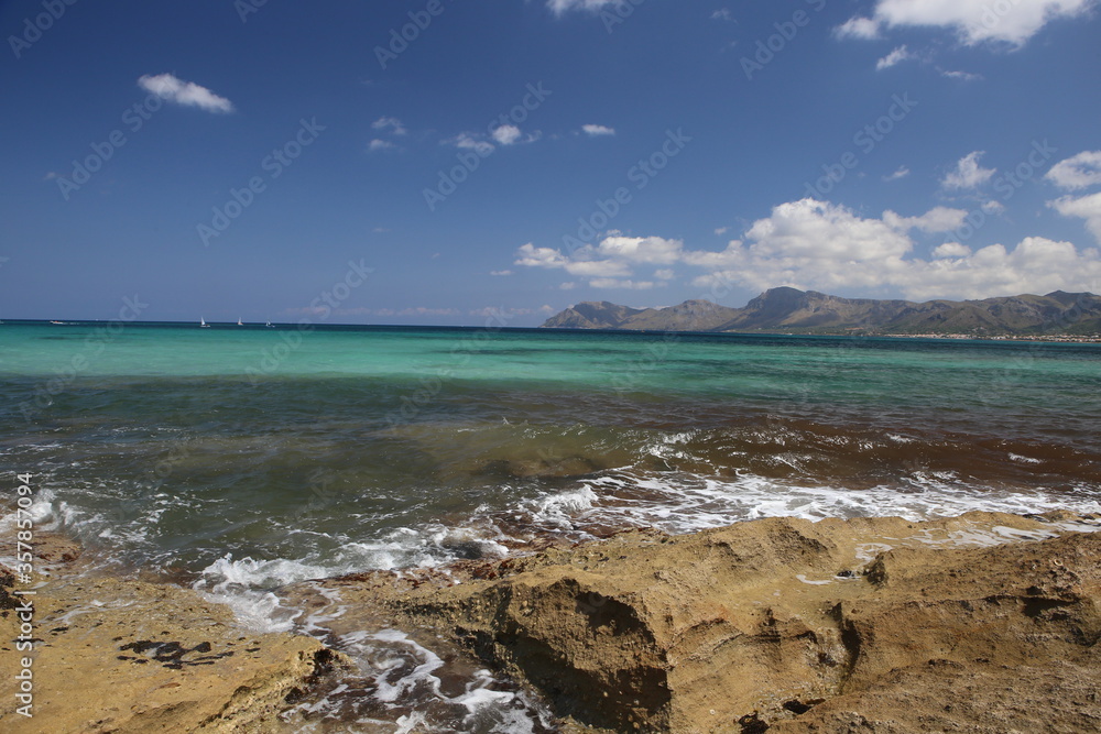 panorama landscape scenic view of isolated deserted yellow rocky beach with blue turquoise sea water and sky with white clouds and mountain background on beautiful and colorful Mallorca island, Spain