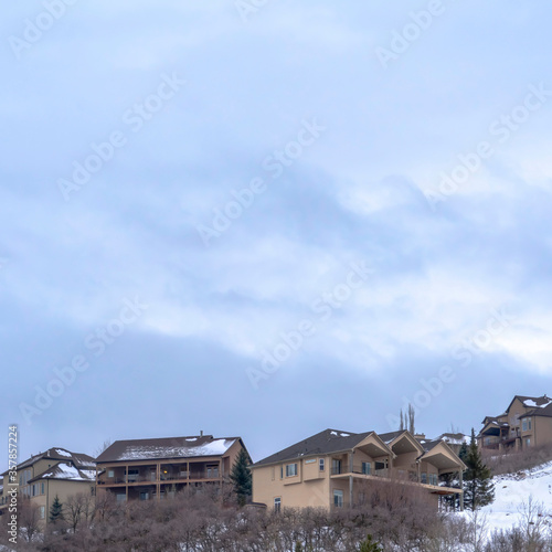 Square Cloudy blue sky over homes atop a hill covered with fresh white snow in winter © Jason