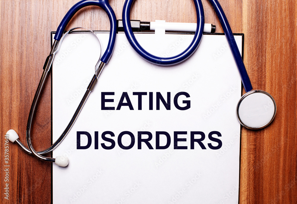 An eating disorder is written on a white sheet that lies on a wooden table near a stethoscope. Medical concept An eating disorder is written on a white sheet that lies on a wooden table near a stethoscope. Medical concept