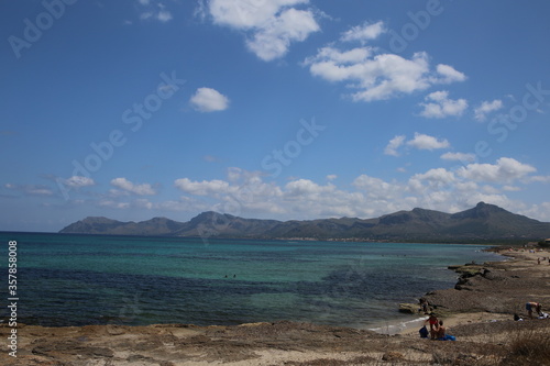 panorama landscape scenic view of isolated deserted rocky beach with blue turquoise sea water and sky with whtile clouds and a mountain background on beautiful and colorful Mallorca island in Spain