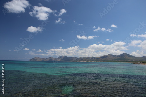 panorama landscape scenic view of blue sea water with underwater rocks and sky with white clouds and mountain background on beautiful and colorful Mallorca island in Spain