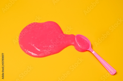 Shot of a blue plastic spoon with pink sticky slime on yellow background. Minimalism in photography, concept creative picture.