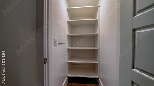 Panorama Walk in closet or pantry with empty wall shelves seen through open hinged door