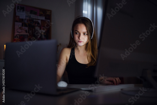 Bored young girl with computer sitting indoors, online chatting concept.