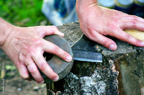 Sharpening an axe. The woodcutter is lying on a stump. One hand holds the touchstone in motion.