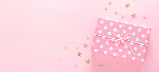 Gift box on a delicate pink background with sparkles, copy space.