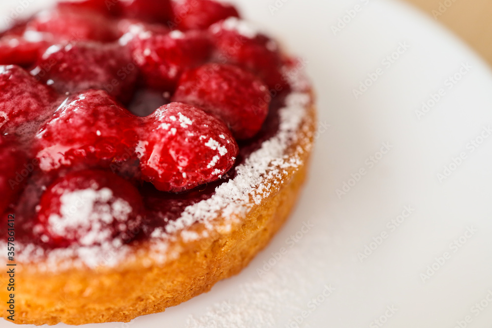 Closeup view of part of a raspberry tart with icing sugar . White plate background. Closeup view of part of a raspberry tart with icing sugar . White plate background.