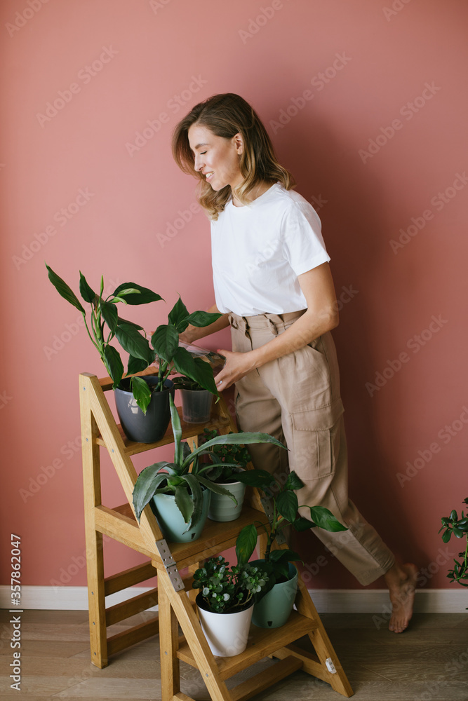 Young woman taking care of plants and home flowers, wearing apron casual stylish clothes. Home gardening. Young woman taking care of plants and home flowers, wearing apron casual stylish clothes. Home gardening.
