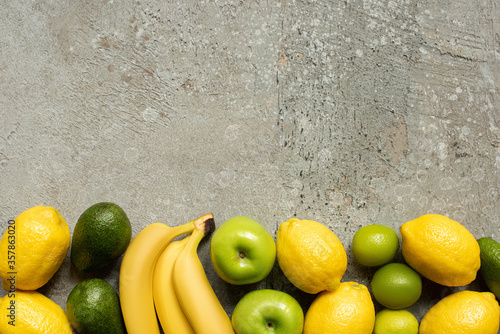 top view of colorful bananas, apples, avocado, limes and lemons on grey concrete surface
